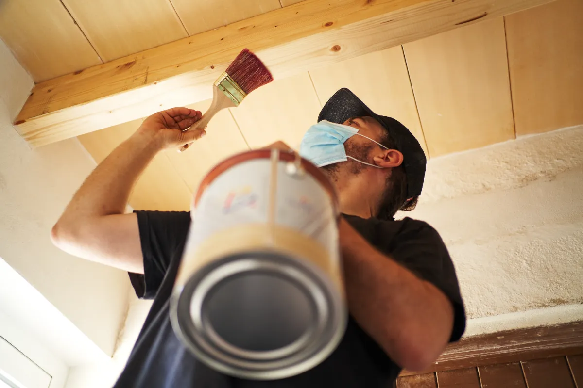 A man applying a coating of paint at the ceiling.